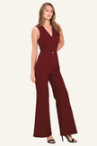 A woman modeling a sleeveless burgundy jumpsuit with a V-neckline, front button placket, and wide-leg pants, photographed against a plain light background.