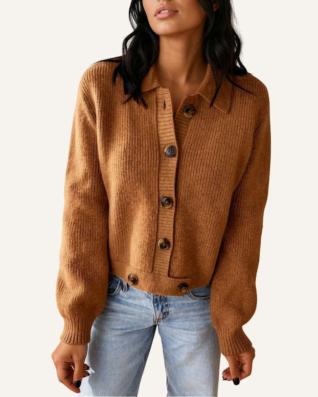 A woman wearing a cropped, ribbed knit cardigan in a warm camel brown color with dark buttons, paired with light-wash blue jeans.