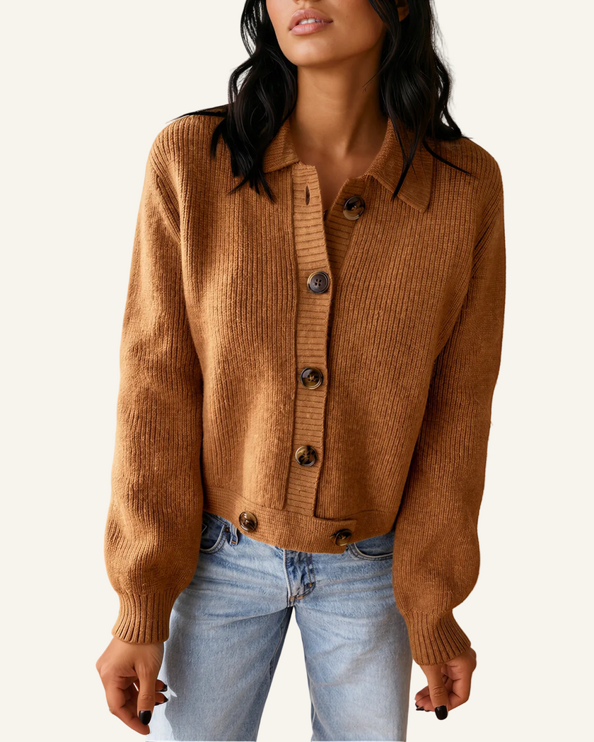A woman wearing a cropped, ribbed knit cardigan in a warm camel brown color with dark buttons, paired with light-wash blue jeans.